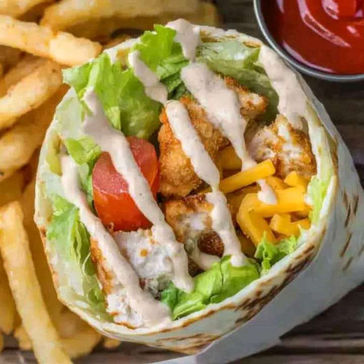 A grilled chicken wrap stuffed with lettuce, tomatoes, avocado, and cheese, drizzled with chipotle mayo.