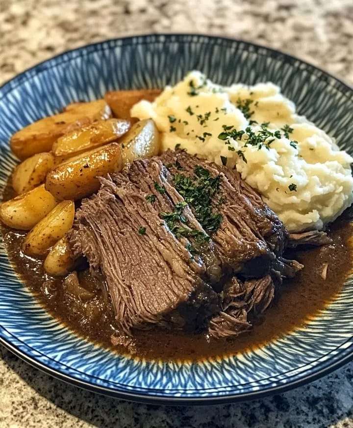 A plate of tender pot roast with carrots, served over creamy mashed potatoes and garnished with fresh parsley.