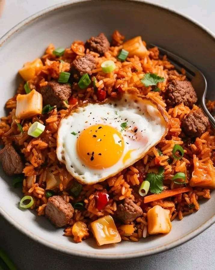 A bowl of beef and kimchi fried rice topped with a fried egg and garnished with green onions.