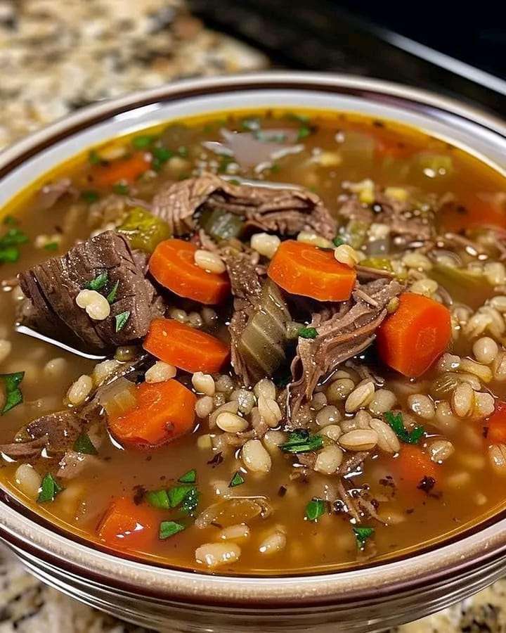 A bowl of hearty beef and barley soup with diced carrots, celery, and fresh parsley garnish.