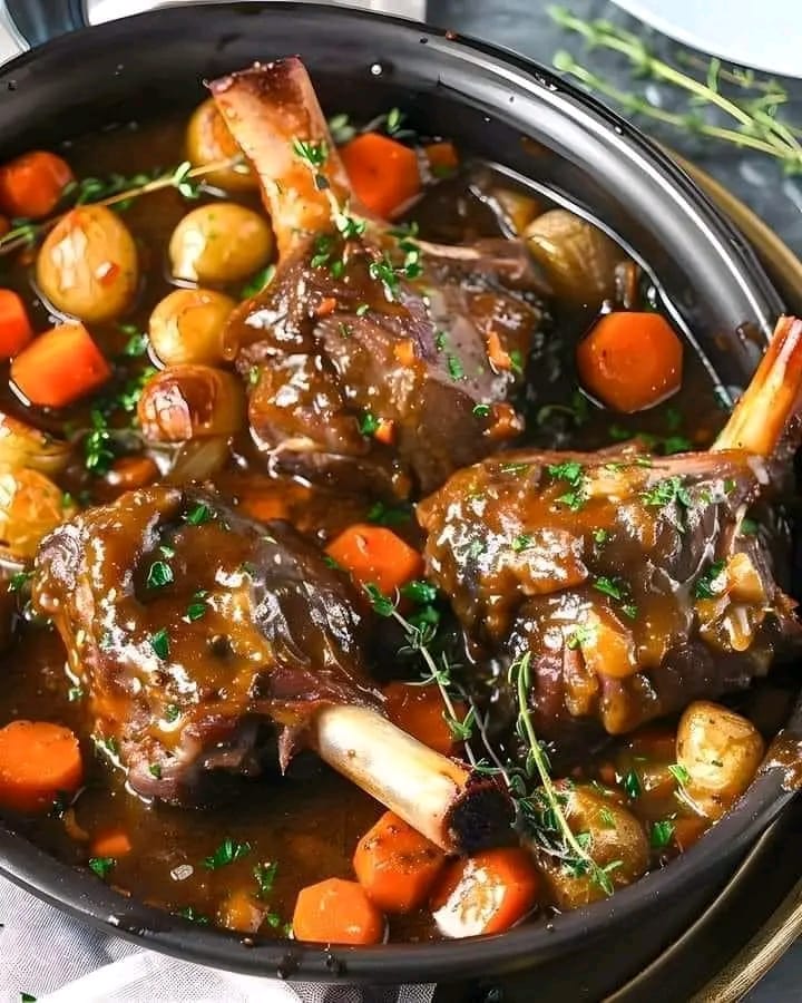 Slow-cooked lamb shanks served with rich herbed gravy, surrounded by vegetables and garnished with fresh rosemary.