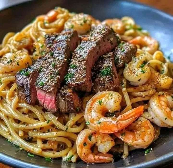 A plate of creamy steak and shrimp pasta garnished with fresh parsley and served with Parmesan cheese on the side.