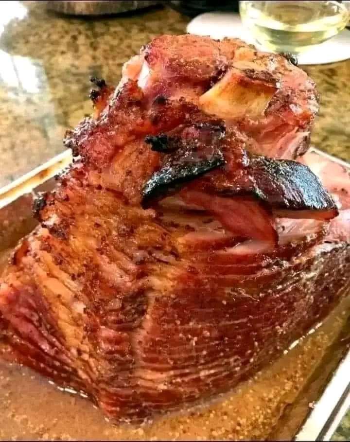 A glazed baked ham with a golden-brown crust, sliced and served on a platter with garnishes.