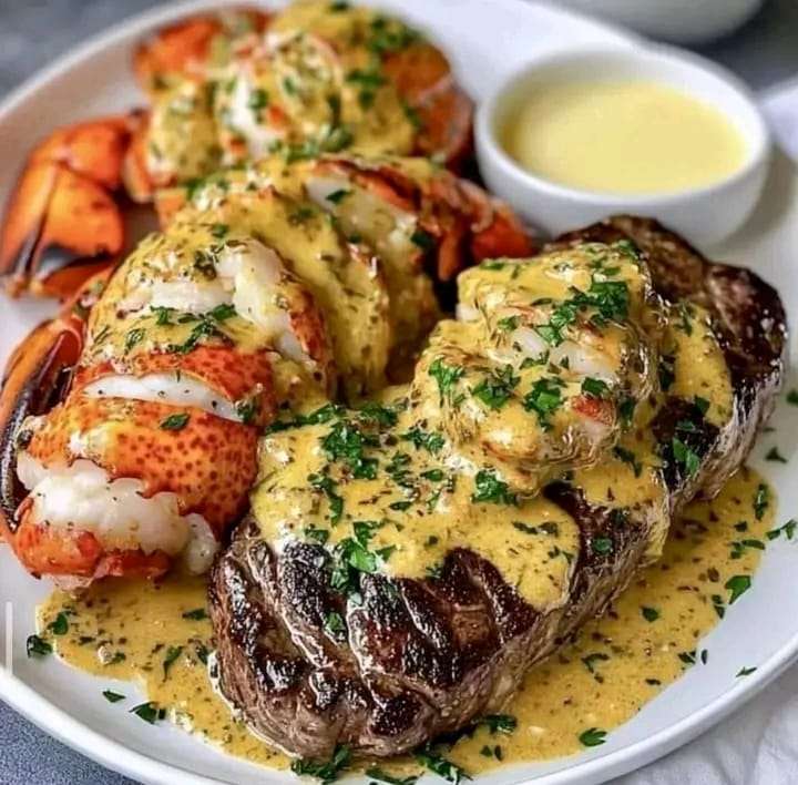 Plate of filet mignon and lobster tail topped with creamy lobster sauce, garnished with parsley.