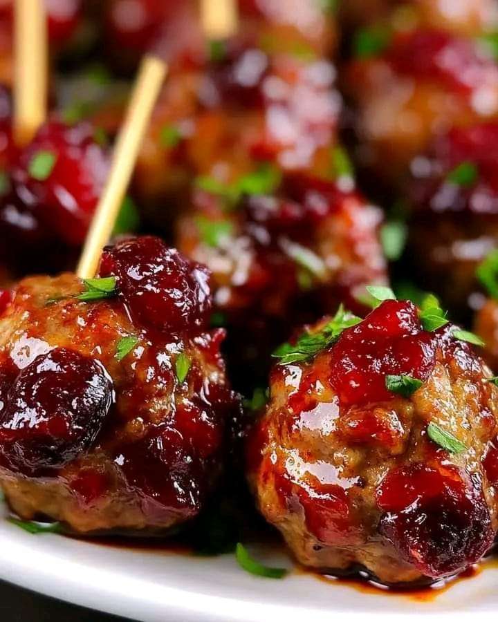 A platter of cranberry meatballs glazed in a shiny cranberry sauce, garnished with parsley, ready to serve.