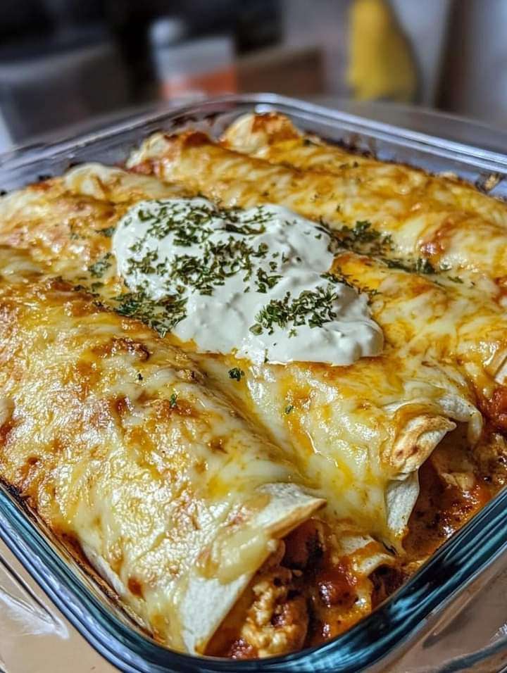 Cheesy chicken enchiladas topped with creamy sauce, melted cheese, and fresh cilantro in a baking dish.