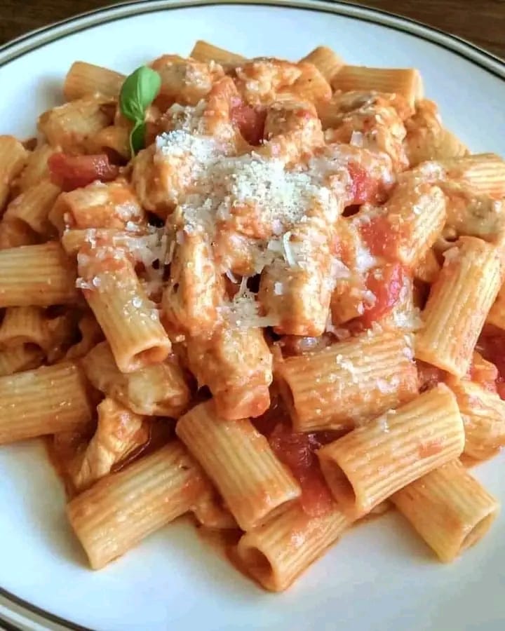 A plate of Chicken Riggies garnished with Parmesan and fresh basil, with rigatoni coated in a creamy tomato sauce.