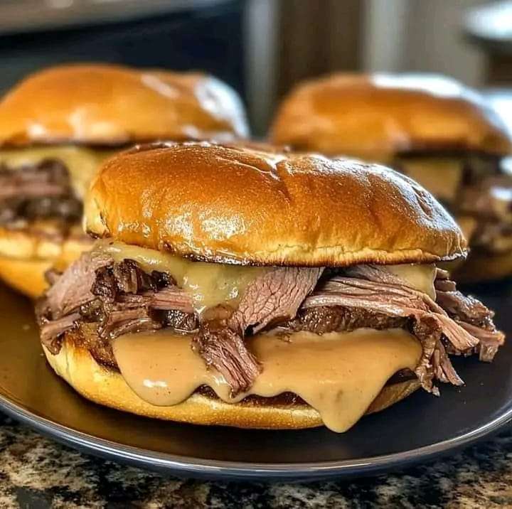 Warm roast beef sandwiches with melted cheese, layered with lettuce and sauce, served on a platter.