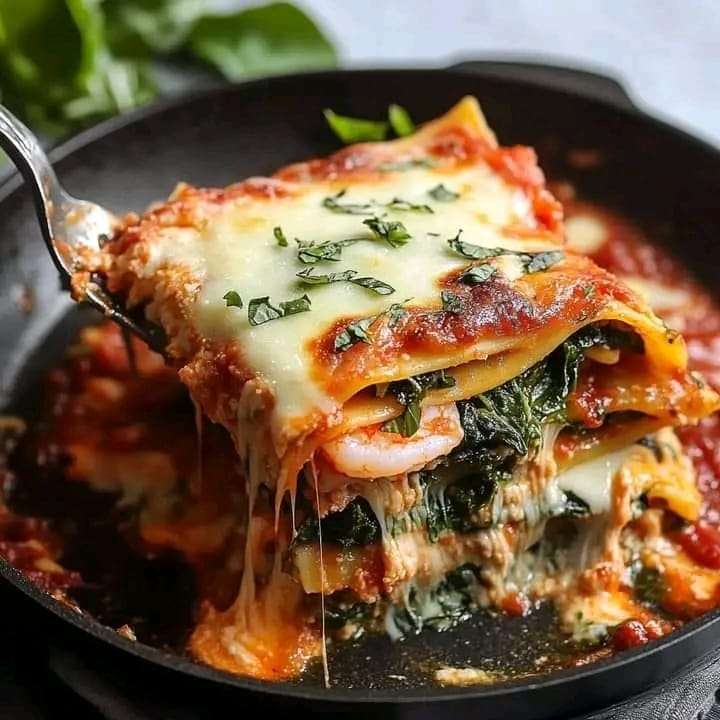 A skillet filled with spinach lasagna topped with melted cheese and fresh basil, served hot and bubbly.