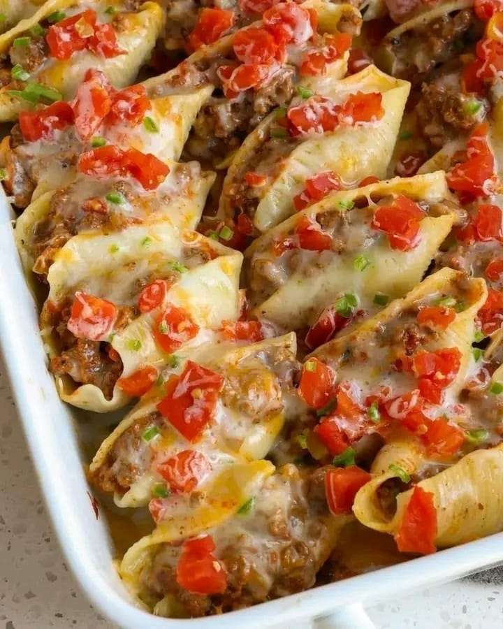 Taco stuffed shells with melted cheese and jalapeño garnish in a baking dish.