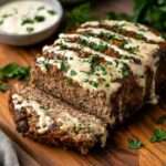 A freshly baked classic meatloaf drizzled with creamy garlic sauce, garnished with fresh parsley.