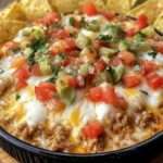 A bubbling dish of Texas Trash Dip topped with melted cheese, green onions, and diced tomatoes.