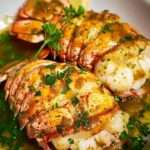 Broiled lobster tails with golden garlic butter and fresh parsley garnish.