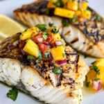 Grilled halibut fillet topped with vibrant mango salsa and garnished with fresh cilantro.