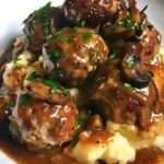 Juicy beef meatballs in a creamy mushroom gravy served with mashed potatoes and garnished with fresh parsley.