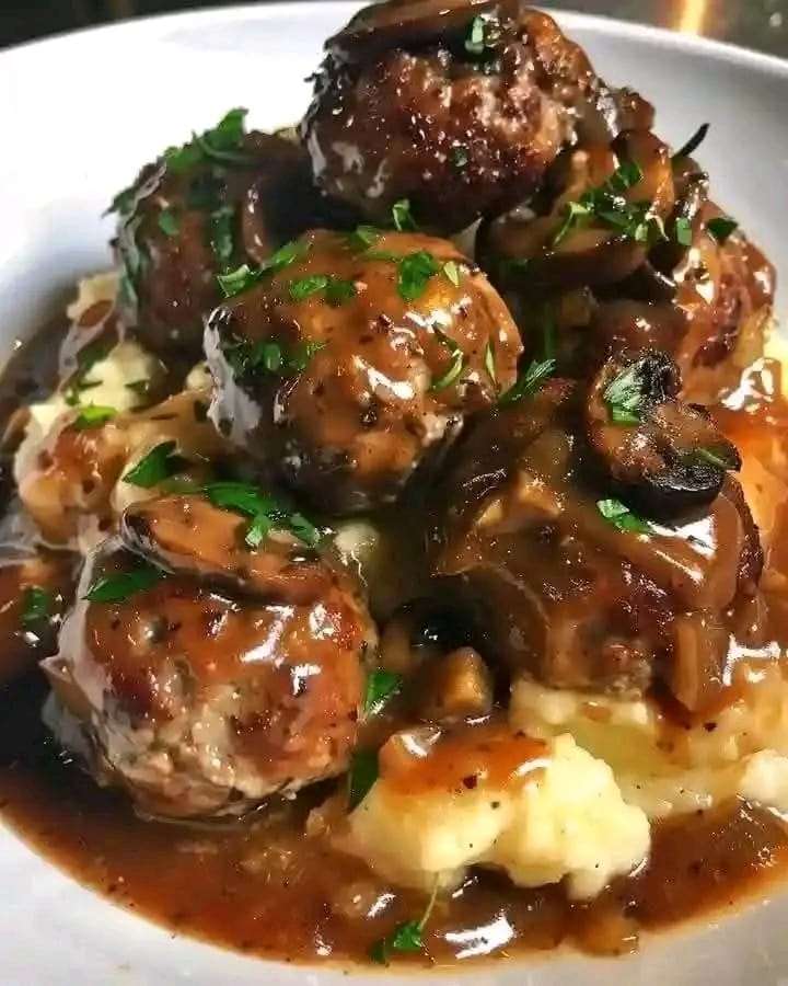 Juicy beef meatballs in a creamy mushroom gravy served with mashed potatoes and garnished with fresh parsley.