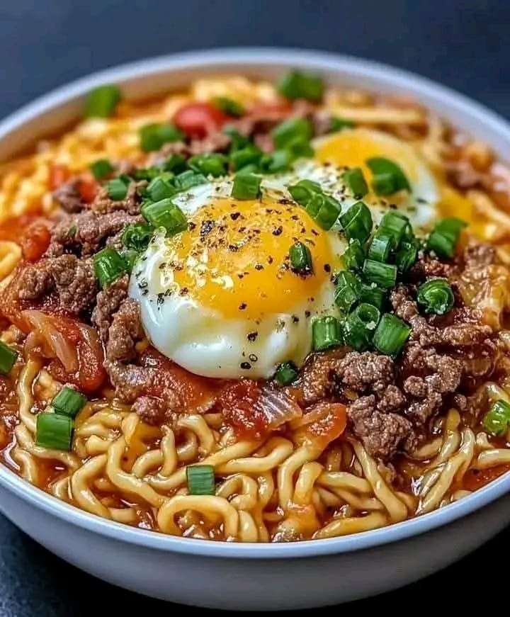 Bowl of Tomato Egg and Beef Noodle Soup topped with bacon, sour cream, and fresh parsley, served with a side of crusty bread.