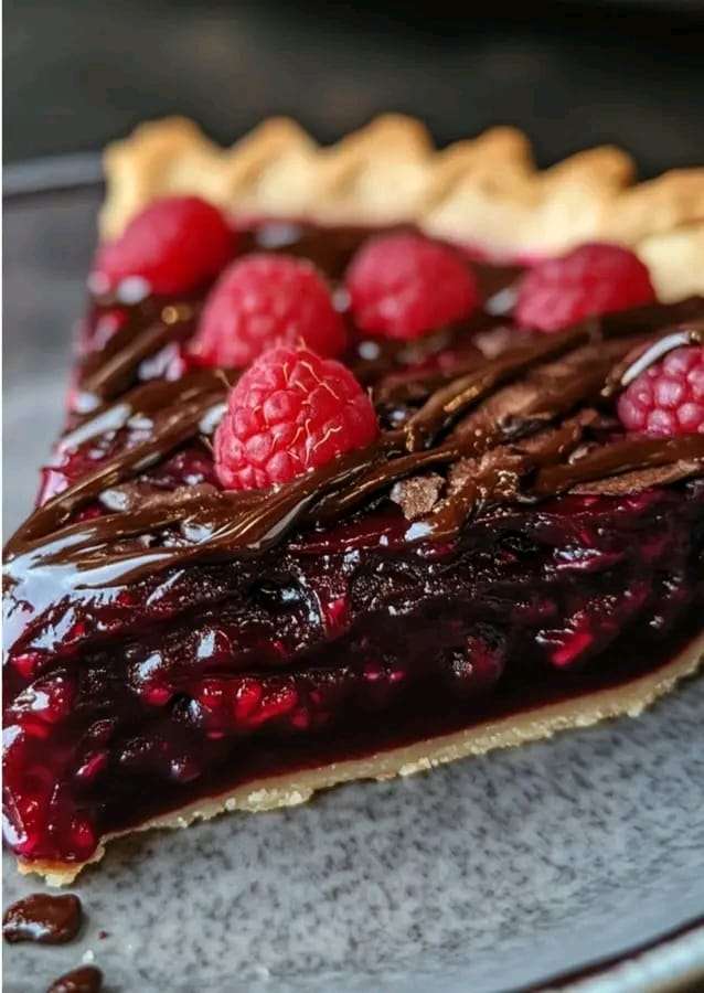 Dark chocolate raspberry pie with glossy ganache, fresh raspberries, and whipped cream topping, served chilled.