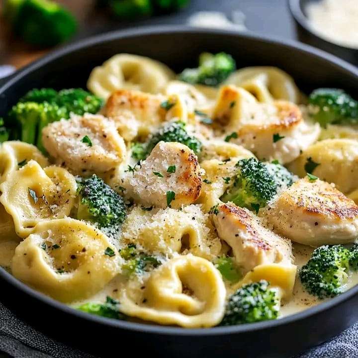 A creamy plate of Garlic Parmesan Tortellini with diced chicken and broccoli, garnished with parsley.