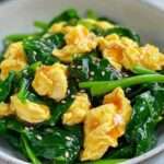 A plate of vibrant Spinach and Egg Stir-Fry garnished with sesame seeds and green onions.