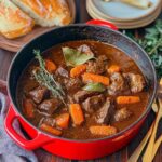 A steaming bowl of hearty beef stew with tender beef chunks, potatoes, and carrots, served in a red cast iron pot. Perfect comfort food for cold nights.