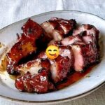 Glazed Char Siu pork sliced on a cutting board with a shiny red glaze.
