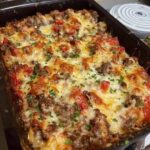 Cheesy baked ground beef and red pepper casserole in a glass baking dish topped with melted mozzarella and cheddar cheese and fresh parsley.