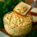 Creamy homemade egg salad spread with shredded carrots and fresh herbs served in a glass bowl with sliced white bread.