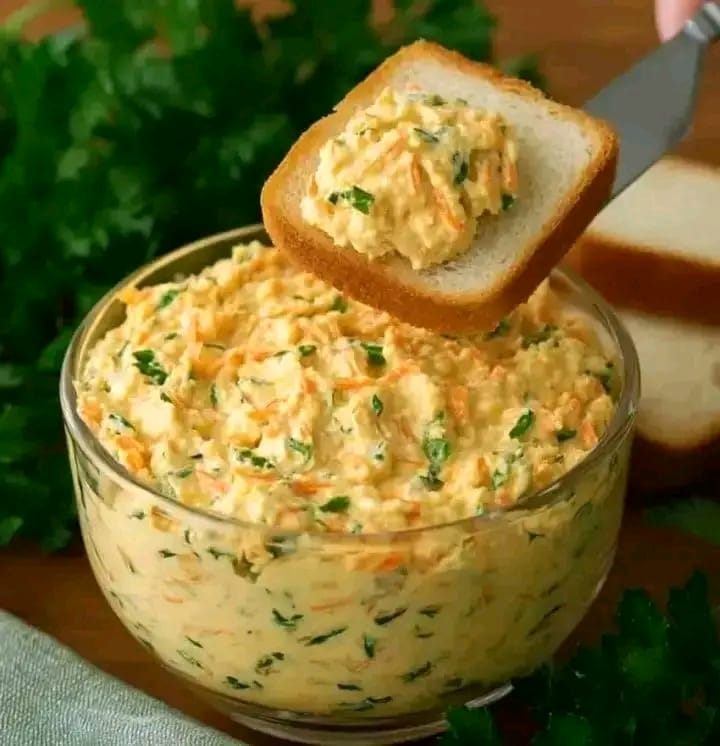 Creamy homemade egg salad spread with shredded carrots and fresh herbs served in a glass bowl with sliced white bread.