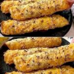 Close-up of golden brown crispy cheese rolls seasoned with black pepper and sesame seeds being held by a hand.