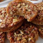 A stack of golden-brown Pecan Pie Muffins showing a chewy interior texture and crunchy pecan topping.