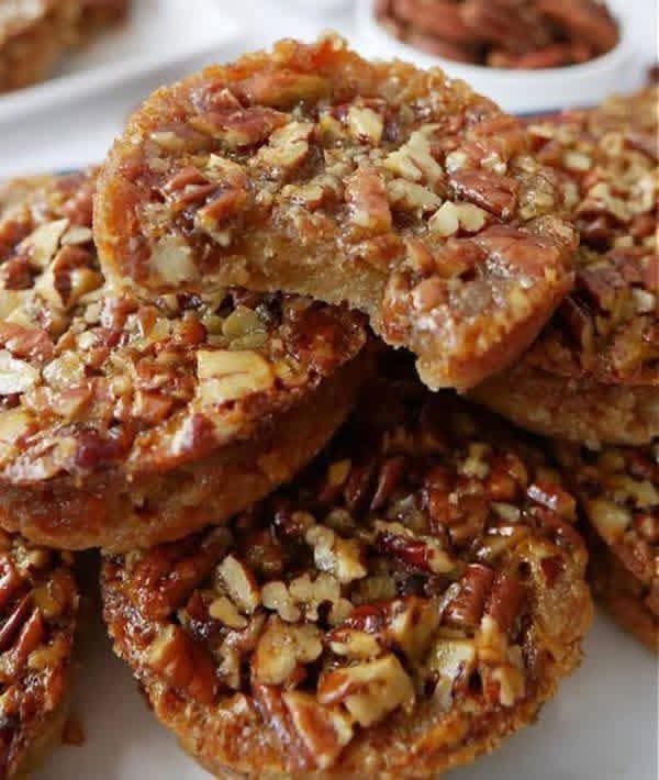 A stack of golden-brown Pecan Pie Muffins showing a chewy interior texture and crunchy pecan topping.