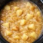 Steaming hot potato and onion stew simmering in a black slow cooker, featuring tender cubed potatoes and translucent onions in a savory golden broth.