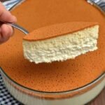 A slice of golden-topped, airy Japanese Soufflé Cheesecake being lifted from a glass baking dish, showing its porous and fluffy interior.