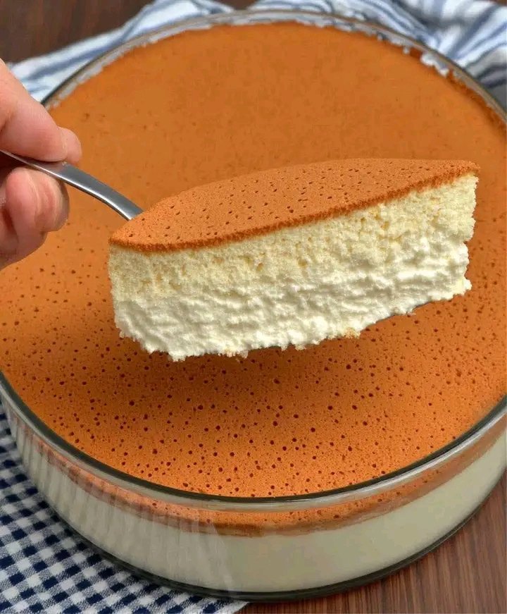 A slice of golden-topped, airy Japanese Soufflé Cheesecake being lifted from a glass baking dish, showing its porous and fluffy interior.