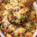 A white ceramic baking dish filled with a cheesy pasta bake featuring ground beef, large pasta shells, green bell peppers, and melted mozzarella.