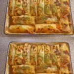 A baking dish filled with golden-brown, oven-baked cabbage rolls topped with fresh herbs and a savory tomato-based sauce.