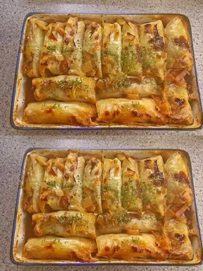 A baking dish filled with golden-brown, oven-baked cabbage rolls topped with fresh herbs and a savory tomato-based sauce.
