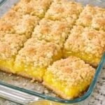 A glass baking dish filled with golden-brown lemon crumble bars, cut into squares, showcasing a vibrant yellow lemon filling and a textured crumb topping.