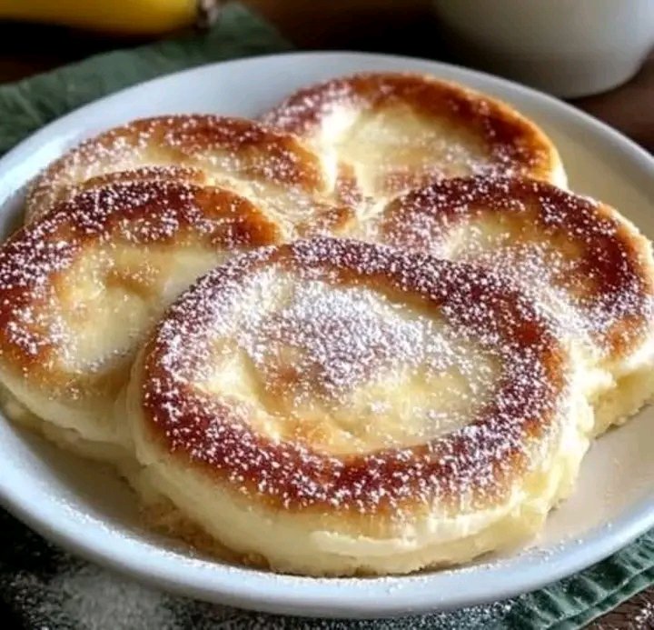 A white plate filled with thick, fluffy golden-brown Japanese soufflé pancakes generously dusted with powdered sugar.
