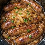 Plump, golden-brown sausages smothered in a mountain of caramelized onions and rich savory gravy inside a black crockpot slow cooker, garnished with fresh parsley.